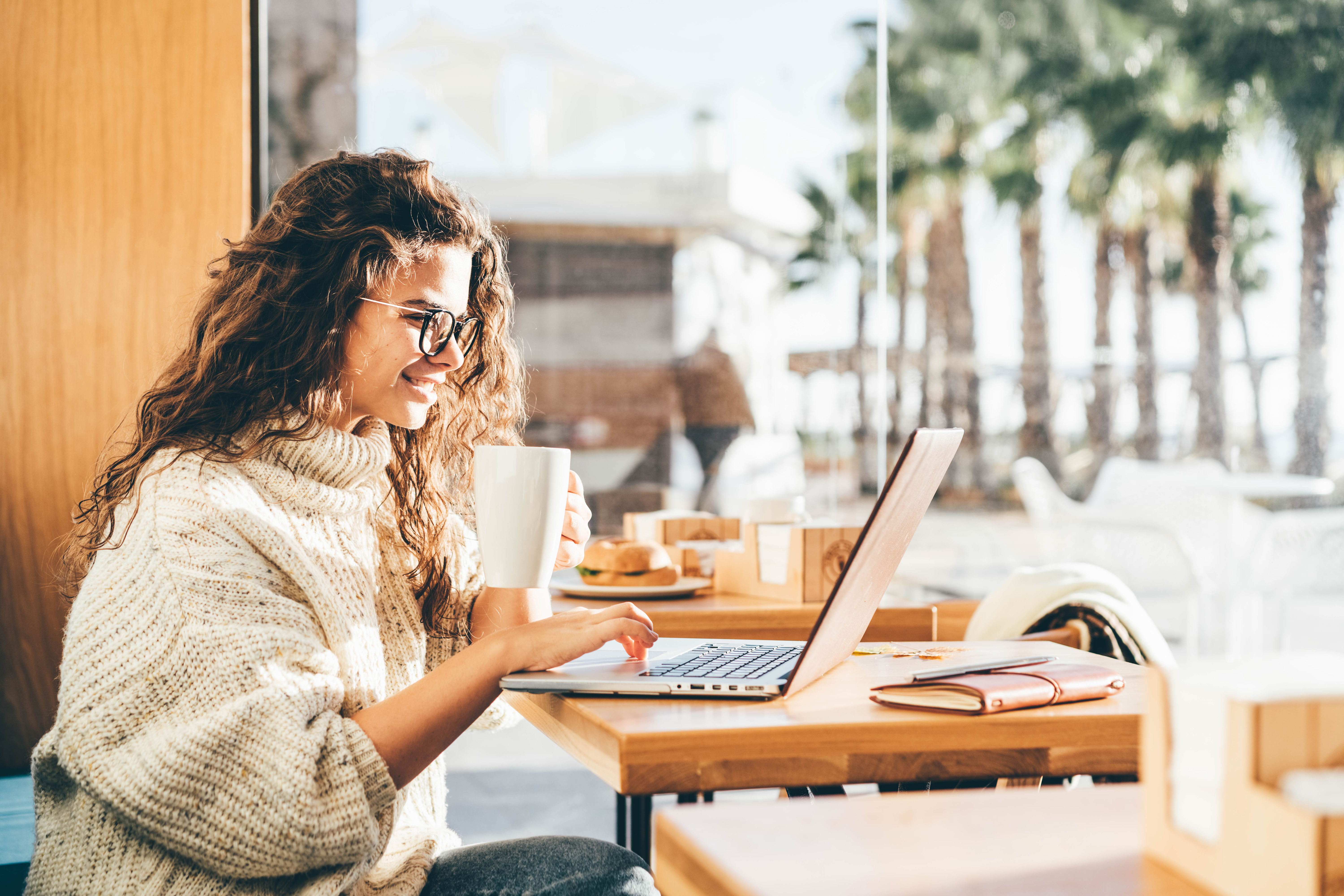 young-woman-sitting-at-caffe-drinking-coffee-and-working-on-laptop