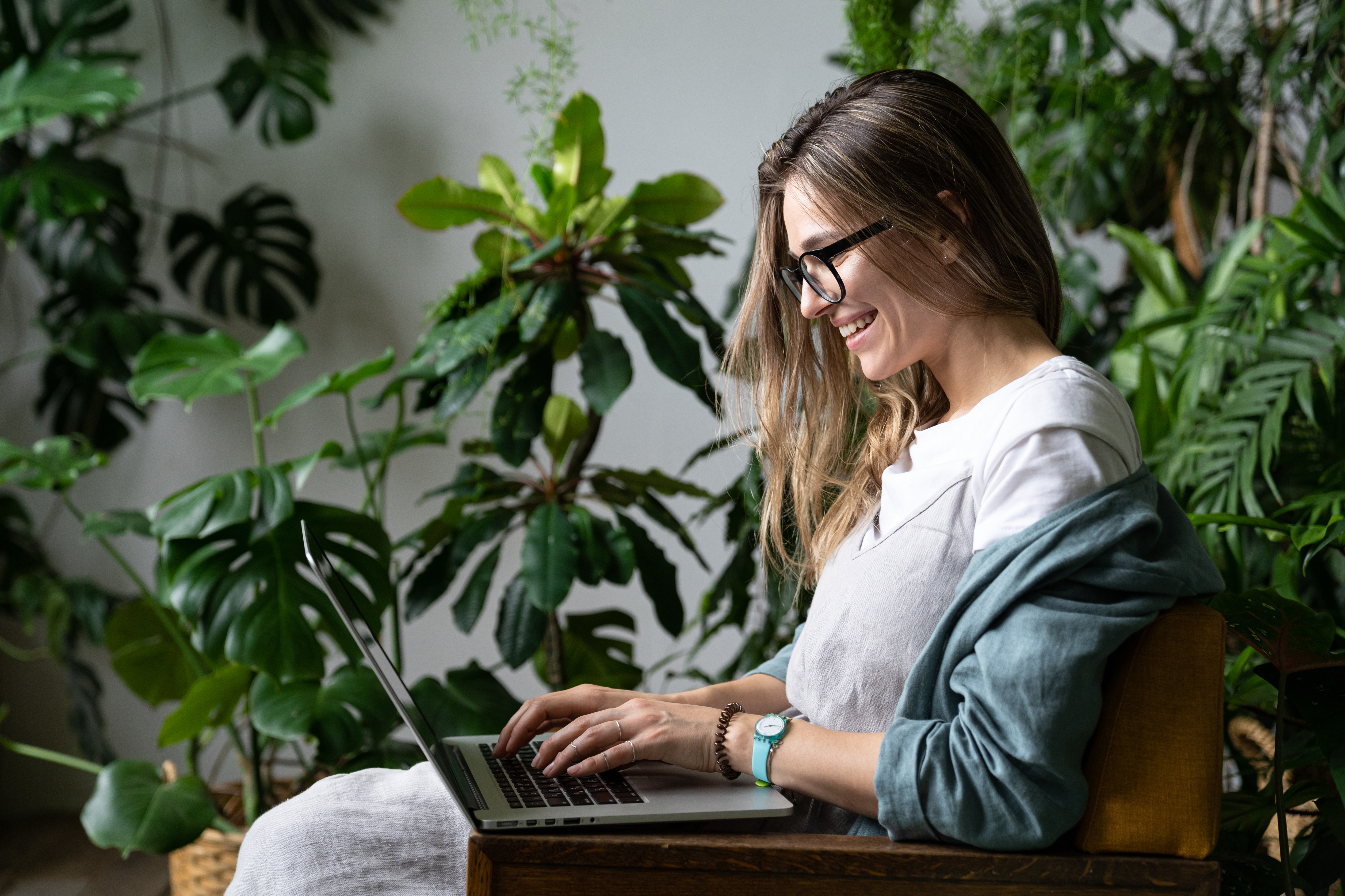smiling-female-gardener-sitting-on-chair-in-green-house-using-l